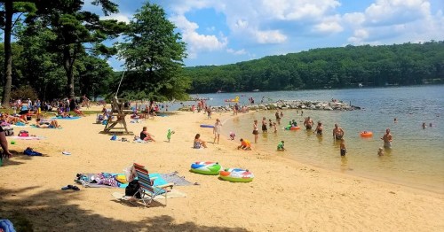 A busy beach scene with people swimming, lounging on the sand, and enjoying the water on a sunny day.