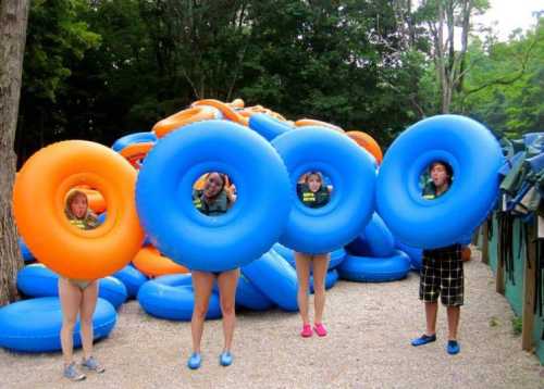 Four people hold large blue and orange inner tubes, standing in front of a pile of more tubes in a wooded area.