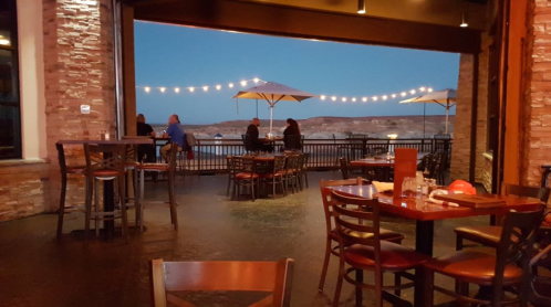 A cozy restaurant interior with empty tables, overlooking a scenic outdoor area with string lights and umbrellas at dusk.