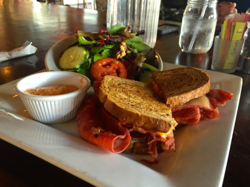 A plate featuring a sandwich with deli meat, served with a side salad and a small bowl of dipping sauce.