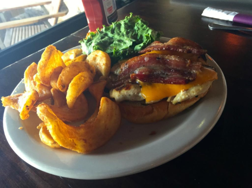 A plate with a cheeseburger topped with bacon, lettuce, and a side of curly fries.