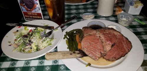 A plate with sliced roast beef, green beans, carrots, and a side salad on a checkered tablecloth.