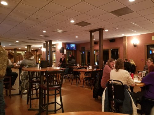 A cozy restaurant interior with wooden tables, patrons dining, and a TV playing in the background.