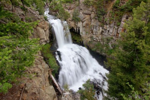 A cascading waterfall surrounded by lush greenery and rocky cliffs, creating a serene natural landscape.