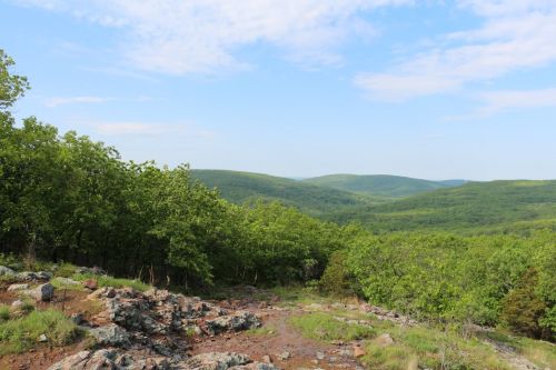 A scenic view of rolling green hills and rocky terrain under a blue sky with scattered clouds.