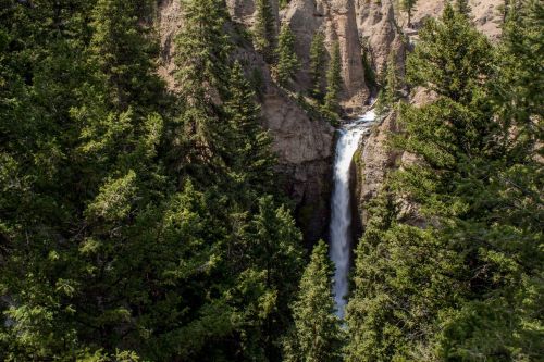 A waterfall cascades down rocky cliffs, surrounded by lush green trees in a scenic natural landscape.