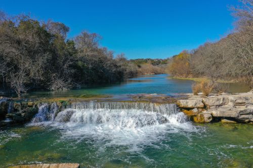 A serene river scene featuring a waterfall, surrounded by trees and clear blue skies.