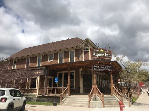 A charming two-story building with a sign reading "Alpine Inn" and a restaurant, set against a cloudy sky.