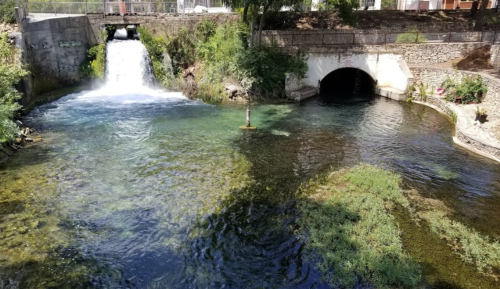 A serene river scene featuring a waterfall, clear water, and lush greenery along the banks.