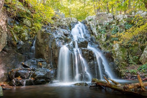 A serene waterfall cascading over rocks, surrounded by lush greenery and autumn foliage.