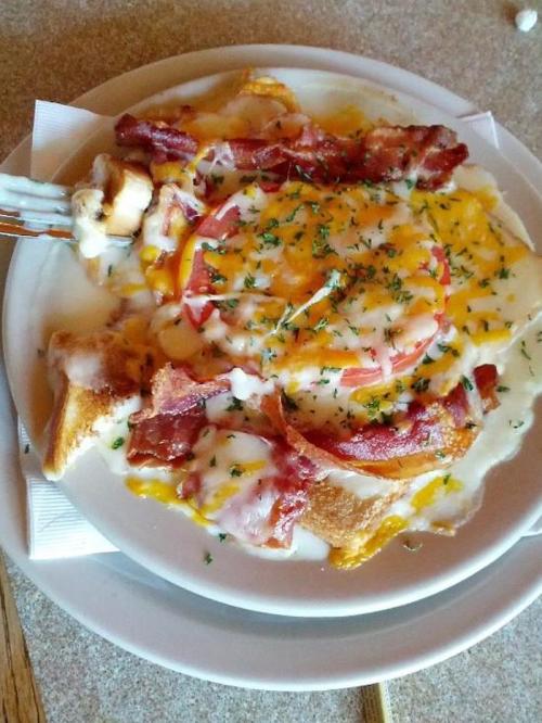 A plate of cheesy breakfast casserole topped with bacon, tomatoes, and herbs.