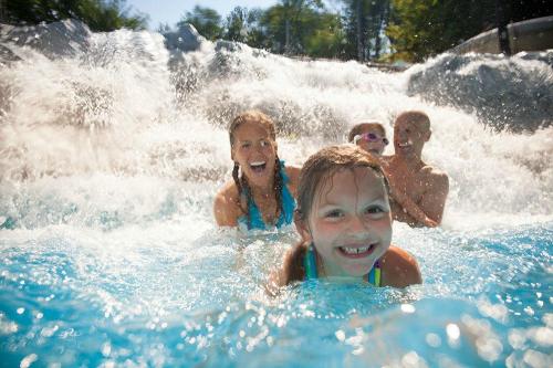 A joyful family splashes in a pool, with kids smiling and water cascading around them.