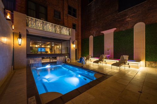 A modern pool area with blue water, lounge chairs, and a glass wall, illuminated by soft lighting in a stylish setting.