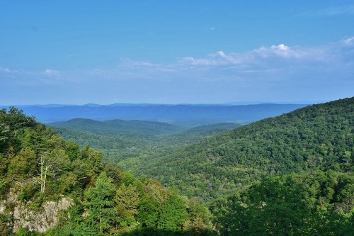 A panoramic view of lush green mountains under a clear blue sky, with rolling hills in the distance.