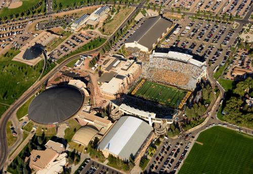 Aerial view of a sports stadium surrounded by parking lots and buildings, with a large crowd in the stands.