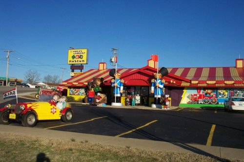 Colorful exterior of a quirky museum with cartoon figures, vintage cars, and a bright sign against a clear blue sky.