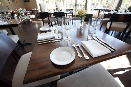A neatly set dining table with plates, cutlery, and glasses in a bright restaurant interior.