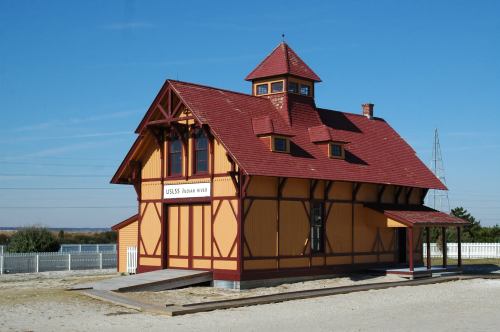Historic train station with a red roof and yellow walls, set against a clear blue sky and surrounded by a white fence.