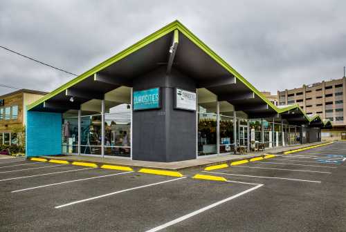 A modern retail building with a distinctive angled roof, featuring large windows and a colorful exterior, in a parking lot.