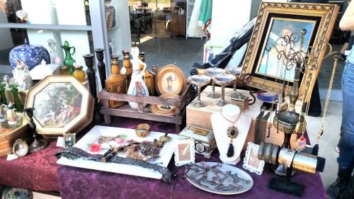A table filled with various antiques, including framed art, bottles, jewelry, and decorative items.