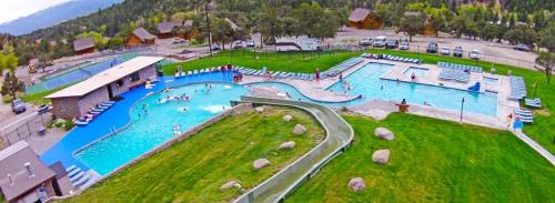 Aerial view of a resort pool area with slides, surrounded by green grass and trees, with people enjoying the water.