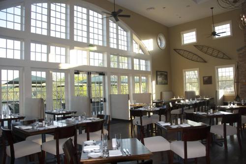 Bright restaurant interior with large windows, wooden tables, and white chairs, featuring a coastal decor theme.