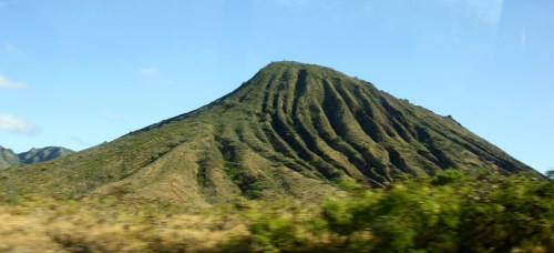 A lush, green volcanic mountain with distinct ridges under a clear blue sky.