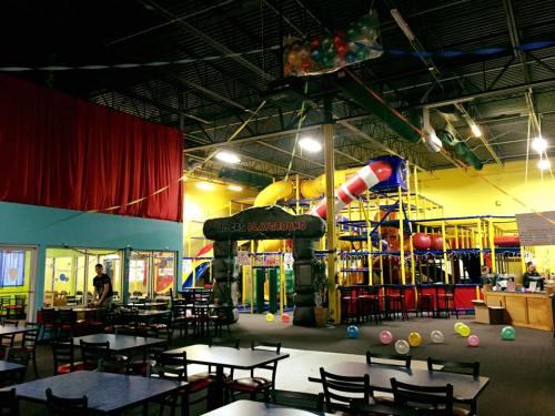 Indoor play area with colorful slides, climbing structures, and tables. Balloons scattered on the floor.