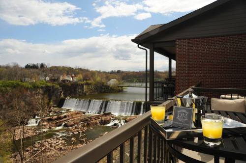 A scenic view from a balcony overlooking a waterfall and river, with drinks on a table in the foreground.