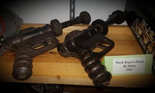Two vintage Buck Rogers pistols from 1936 displayed on a wooden shelf, with a label indicating their origin.