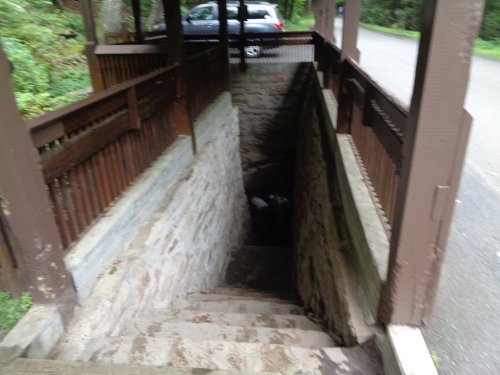 A stone staircase leads down into a dark area, surrounded by wooden railings, with a car parked nearby.