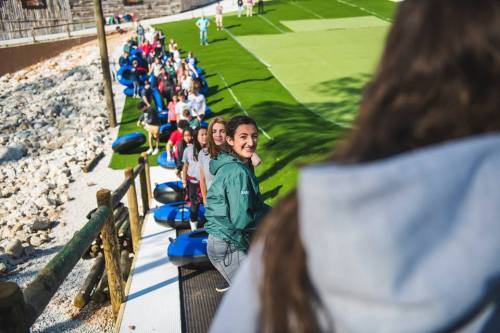 A line of people waiting on a grassy area, with some smiling and others looking ahead, ready for an activity.