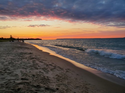 A serene beach at sunset, with gentle waves lapping the shore and colorful clouds reflecting on the water.