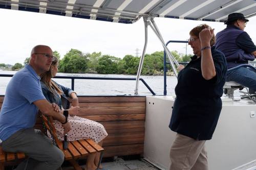 A group of people on a boat, with two sitting and one standing, enjoying a scenic view on the water.