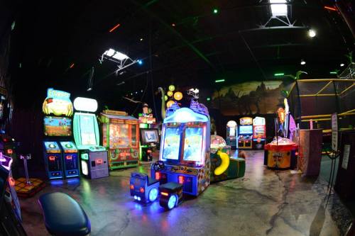 A vibrant arcade filled with colorful game machines and neon lights in a spacious, dimly lit environment.