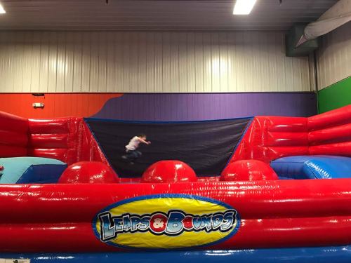 A colorful inflatable bounce area with a large trampoline and a child jumping in the center.
