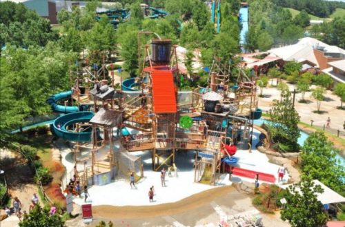 Aerial view of a water park featuring slides, play structures, and people enjoying the attractions amidst greenery.
