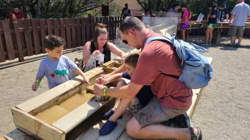 A family enjoys a hands-on activity, sifting through water and sand at an outdoor educational site.