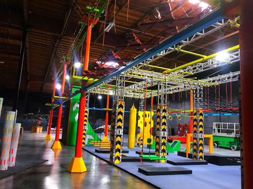 Indoor obstacle course featuring colorful climbing structures, ropes, and various challenges in a spacious arena.