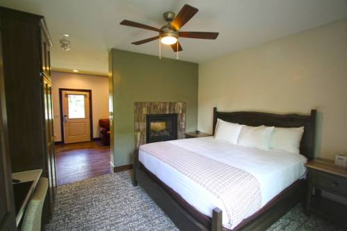 Cozy bedroom featuring a large bed, ceiling fan, fireplace, and a door leading to another room.