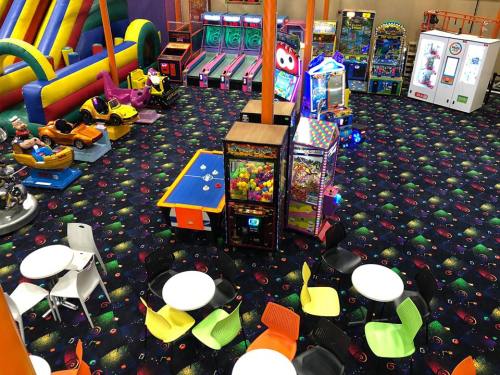 A colorful indoor play area with arcade games, rides, and tables surrounded by vibrant carpet.