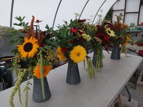 A table with four vases filled with vibrant, mixed flower arrangements, including sunflowers and greenery.