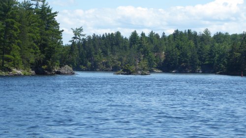A serene lake surrounded by lush green trees and rocky shores under a partly cloudy sky.