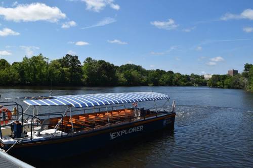 A boat named "Explorer" with a striped canopy floats on a calm river surrounded by lush greenery and blue skies.