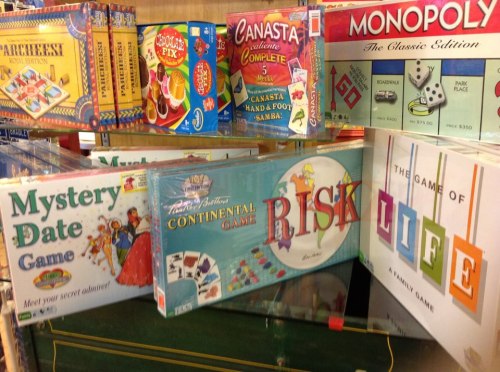 A display of various board games, including Monopoly, Risk, and The Game of Life, on a store shelf.