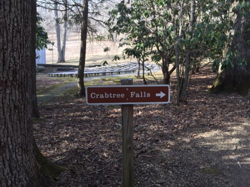 A wooden sign pointing to Crabtree Falls, surrounded by trees and a trail in a natural setting.