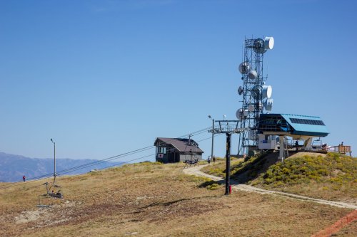A ski lift station and communication tower on a grassy hill under a clear blue sky.