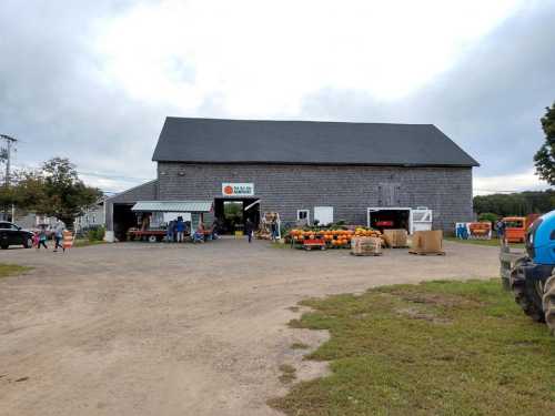 A rustic farm building with a sign, surrounded by pumpkins and people, on a cloudy day.