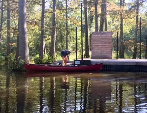 A person in a canoe near a wooden dock surrounded by trees and calm water.