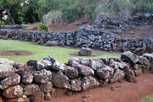 Stone walls and structures in a grassy area, surrounded by trees and vegetation.